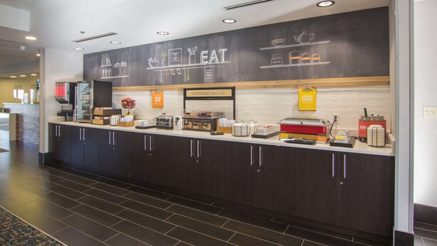 A breakfast bar with a chalkboard menu, kitchen appliances, and a sign indicating breakfast starts here. - Hampton Inn Medina (Medina)