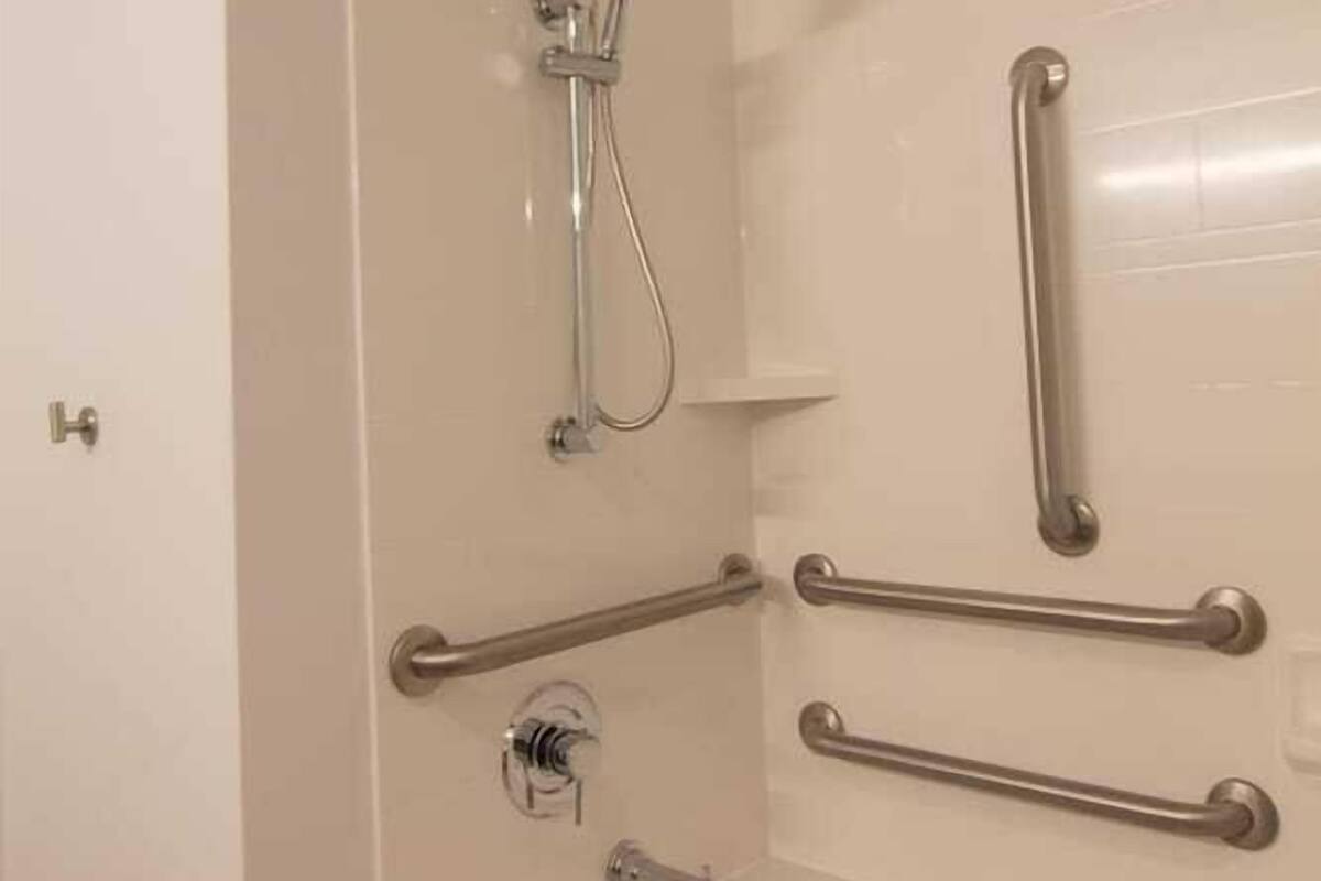 A bathroom with a bathtub, a shower, and handrails.