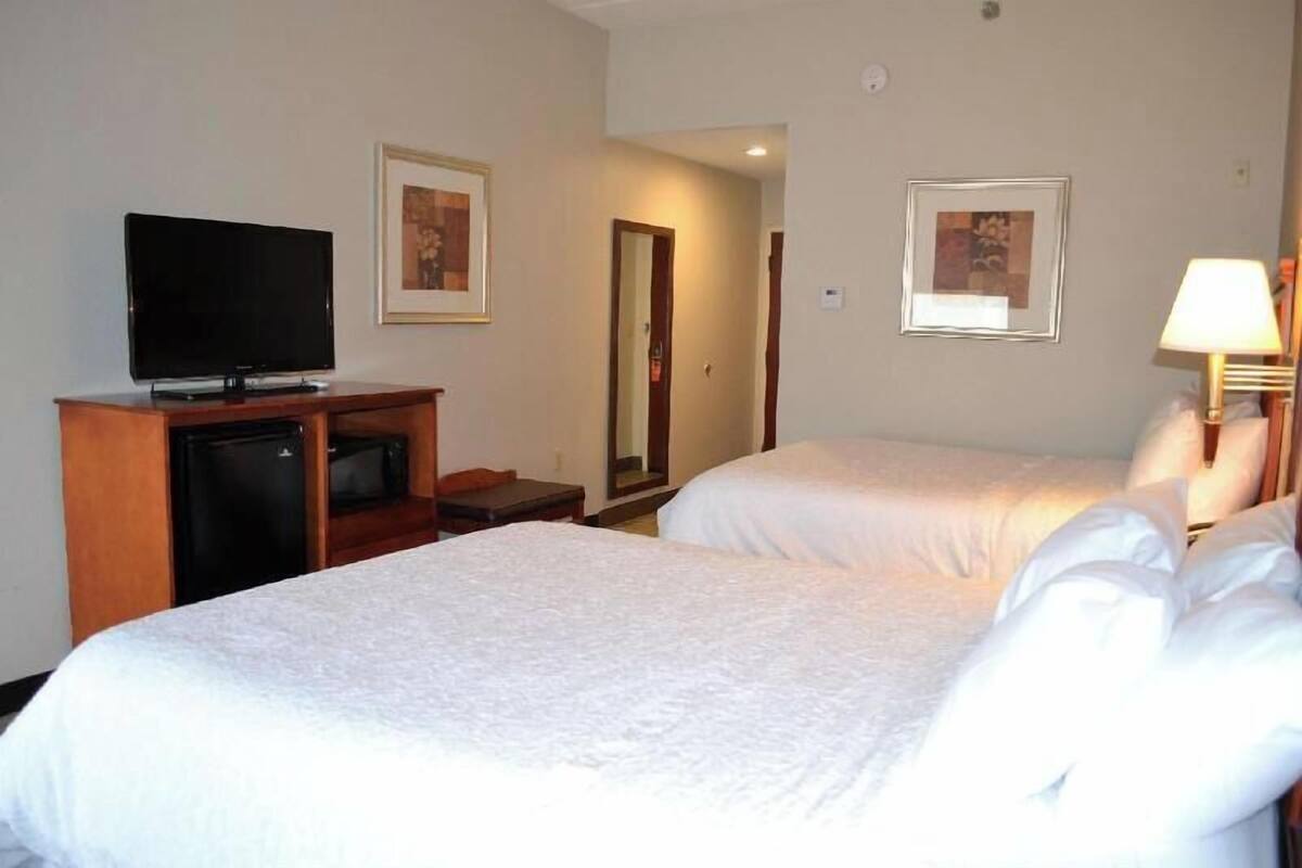 A hotel room with two beds, a television, a desk, and a lamp.