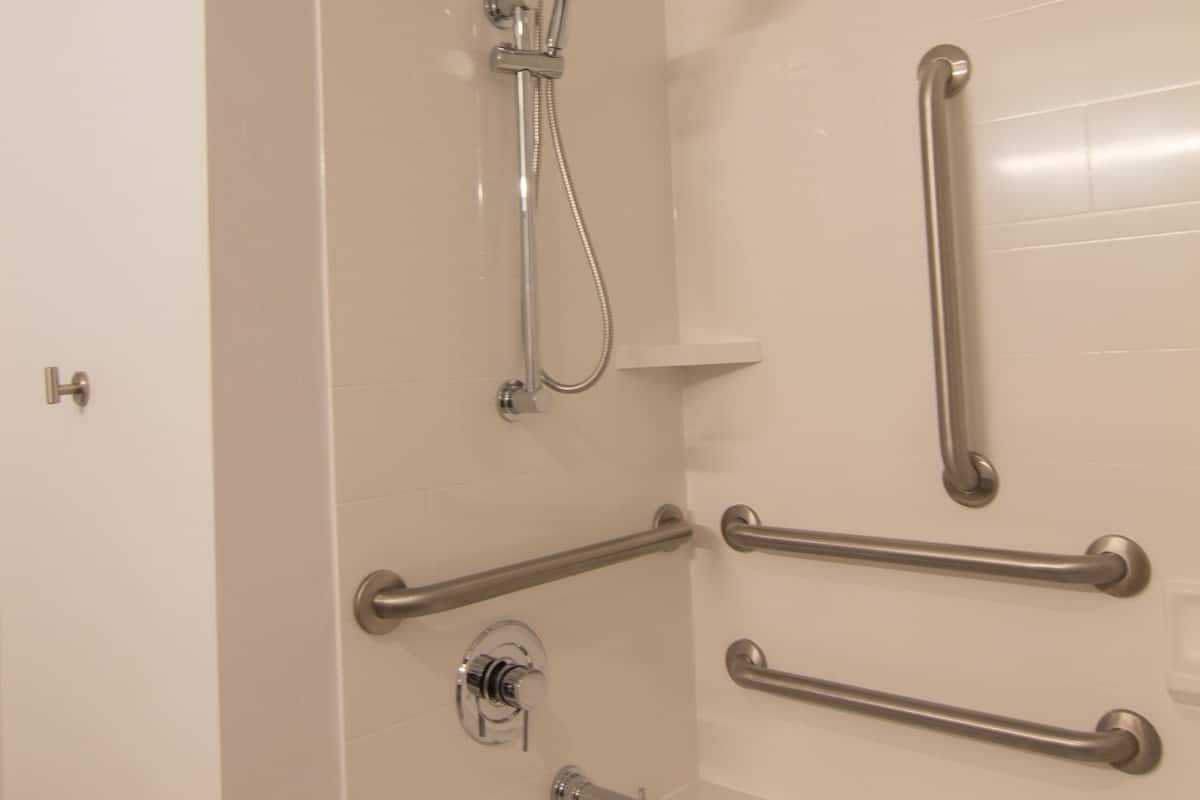 A bathroom with a bathtub, a shower, and handrails.