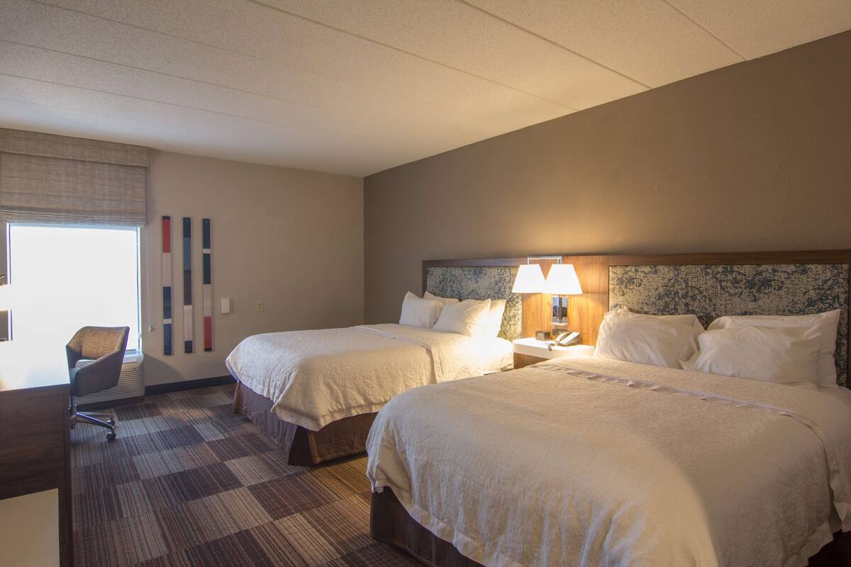 A hotel room with two beds, a desk, and a chair.