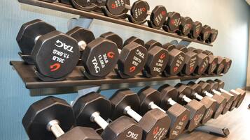 A rack of dumbbells with weight labels, arranged on shelves in a gym setting.