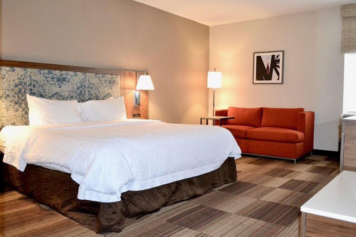 A hotel room with a large bed, a red sofa, a desk, and a lamp.