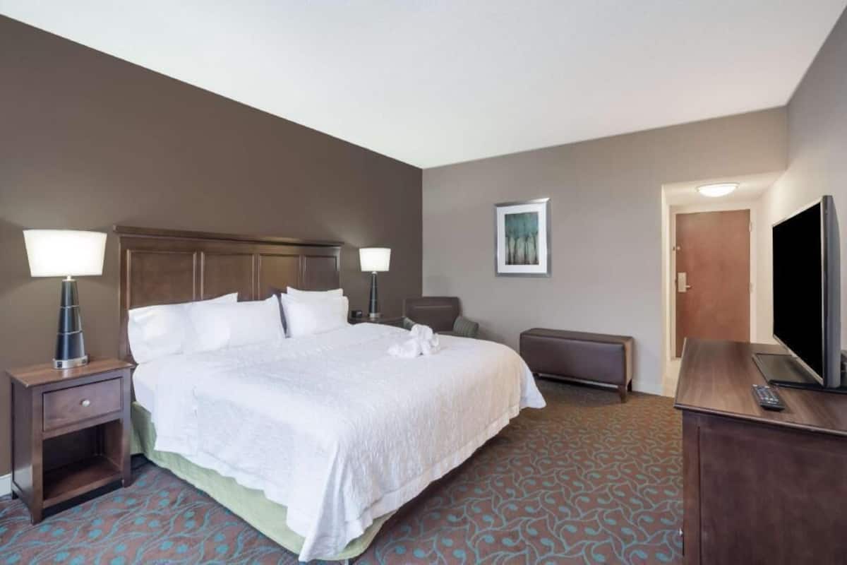 A hotel room with a bed, bedside lamps, a television, a desk, and a door.
