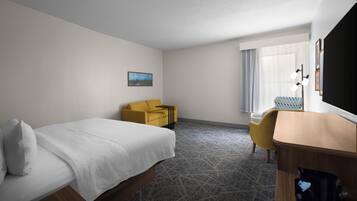 A hotel room with a bed, a desk, a chair, a small table, a picture on the wall, and a window with curtains.