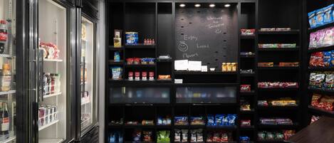 Um bar de lanches com prateleiras cheias de diversos petiscos e bebidas, uma lousa com a inscrição 'Bem-vindos a Terre Haute' e uma geladeira Coca-Cola.