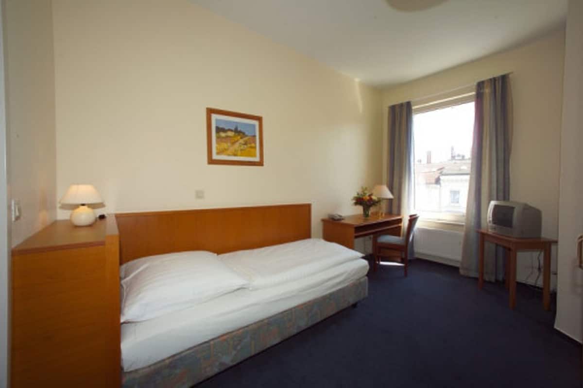 A hotel room with a bed, a desk, a chair, a television, and a window with curtains.