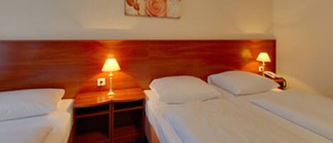 Habitación de hotel con dos camas individuales, cabeceros de madera, mesitas de noche con lámparas y una obra de arte en la pared.