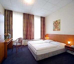A hotel room with a bed, a desk, a chair, and a nightstand with a lamp. - Hotel Terminus am Hauptbahnhof & ZOB (Hamburg)