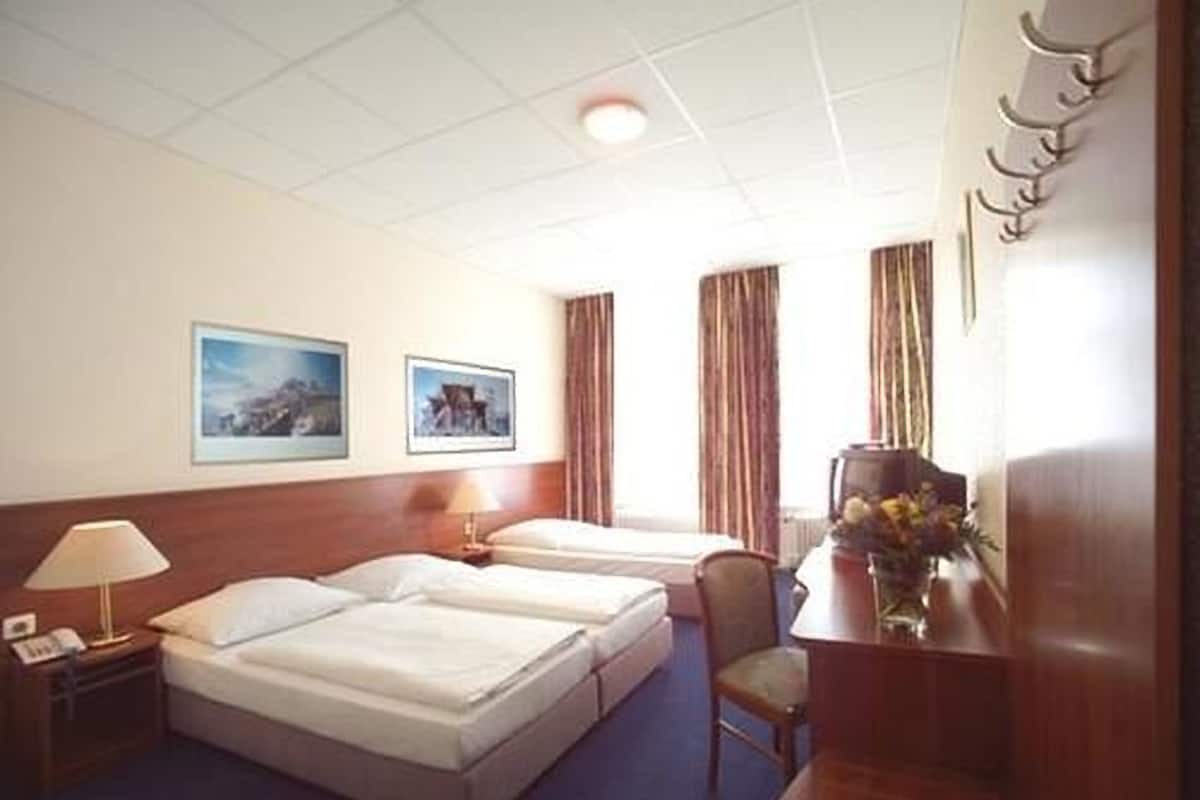 A hotel room with two beds, a desk with a lamp, a chair, and two framed pictures on the wall.