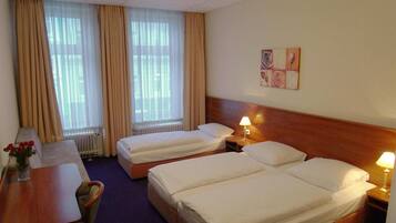 A hotel room with two beds, a desk with a chair, a lamp, and a window with curtains.