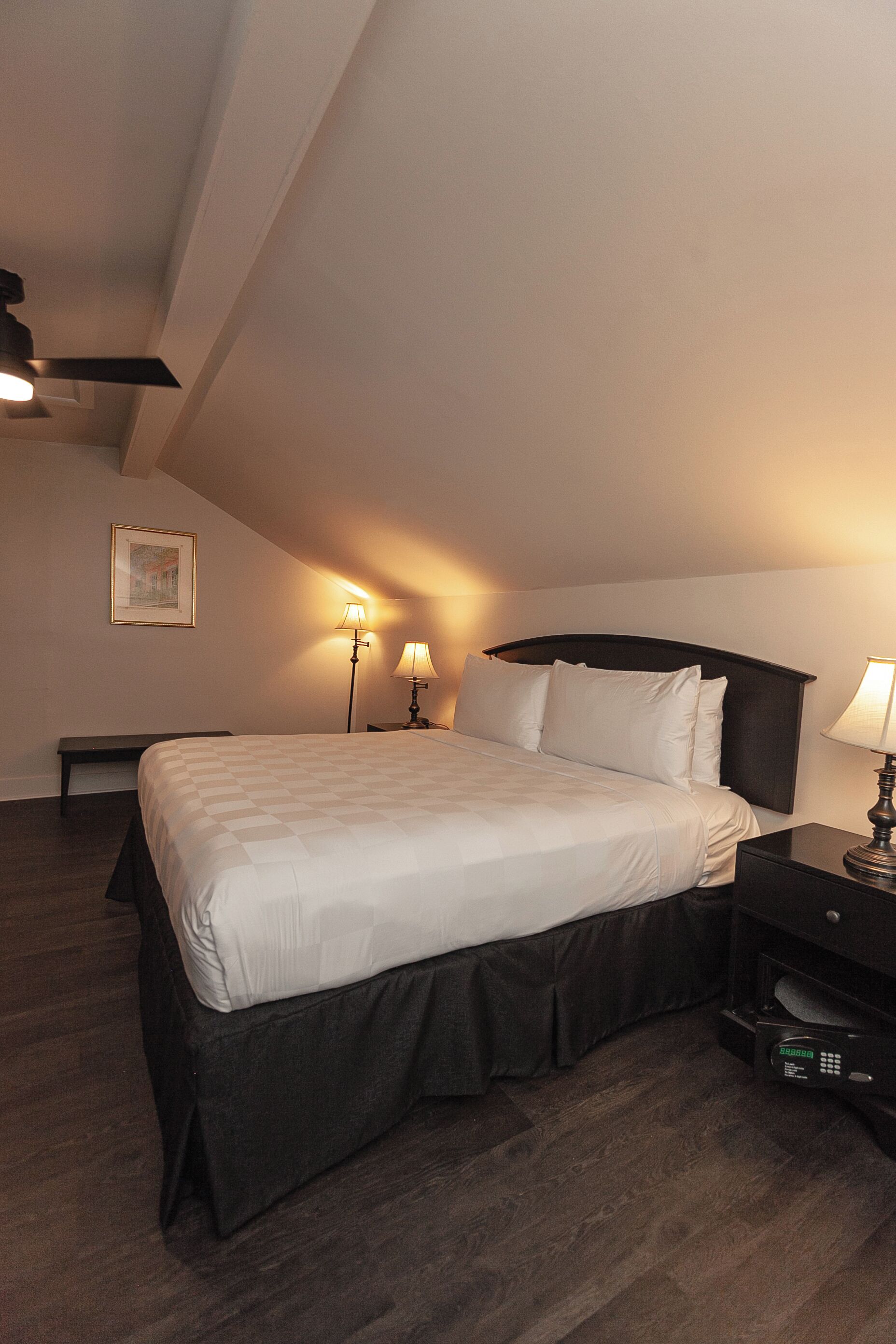 Un lit bien fait dans une pièce dont le plafond est en pente, une table de chevet avec une lampe et un banc adossé au mur.