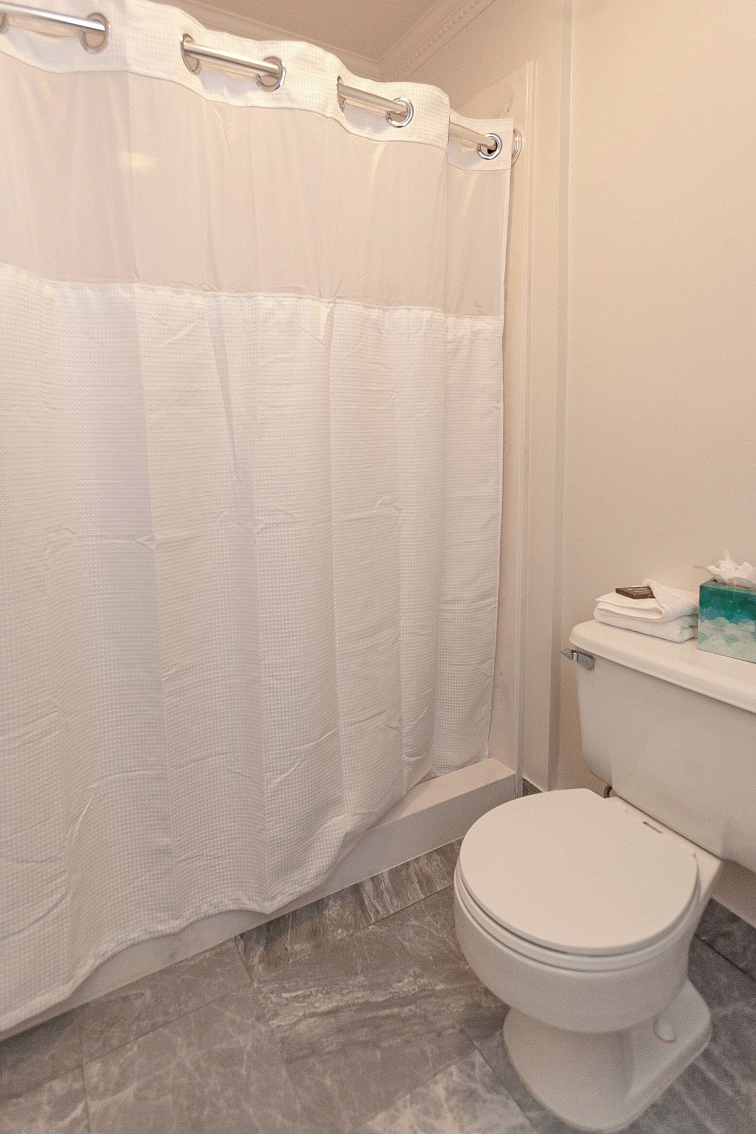 Een badkamer met een witte douchegordijn, een toilet en een klein plankje met toiletartikelen.