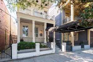 A two-story building with a covered porch, a brick wall on the left, and a white fence with greenery. - The Carriage House on St. Charles (New Orleans)