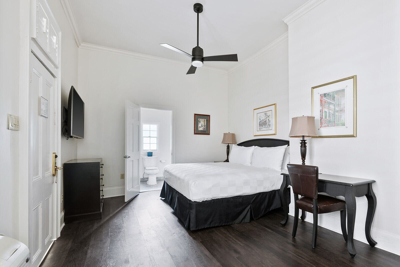 A hotel room with a bed, desk, chair, television, and a ceiling fan.