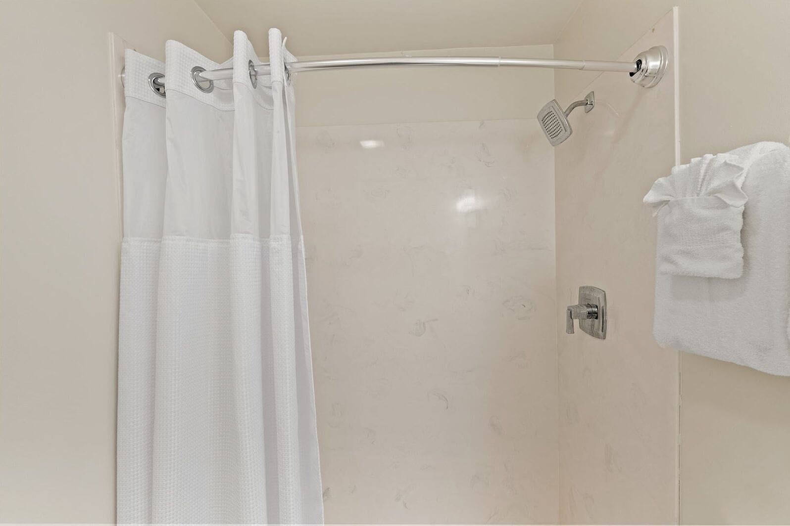 Ducha con mampara de vidrio, cabezal de ducha de mano y toallero con una toalla doblada.