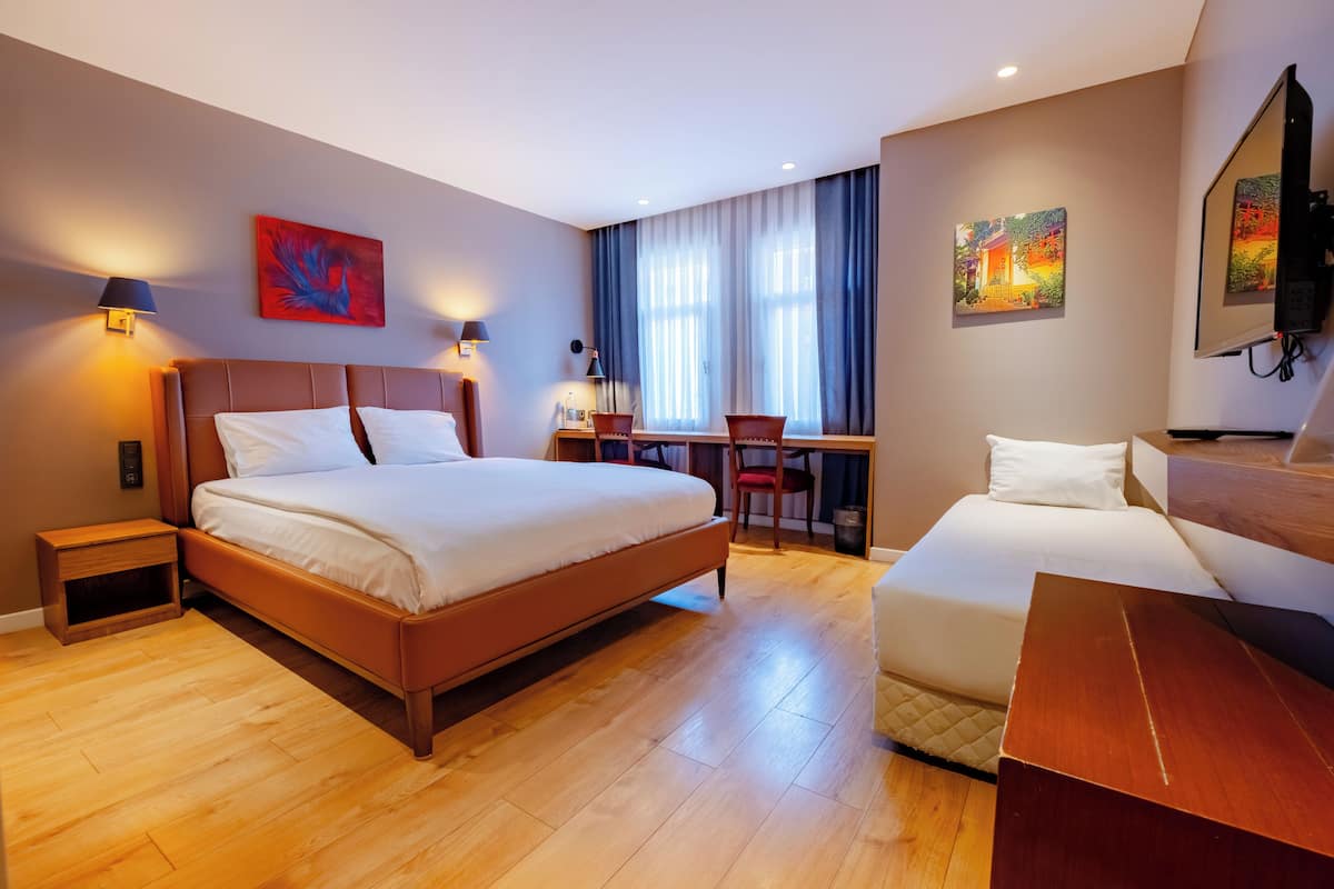 Habitación de hotel con una cama grande, un sofá más pequeño, un escritorio con una silla y obras de arte en las paredes.