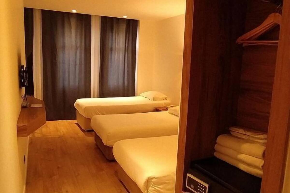 Habitación de hotel con dos camas, piso de madera, cortina oscura y un estante con toallas dobladas.