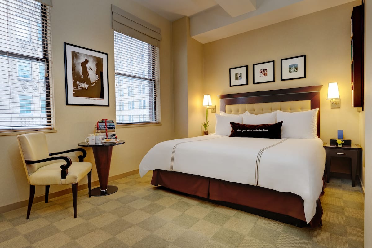 A hotel room with a large bed, a chair, a small table with books, and three framed pictures on the wall.