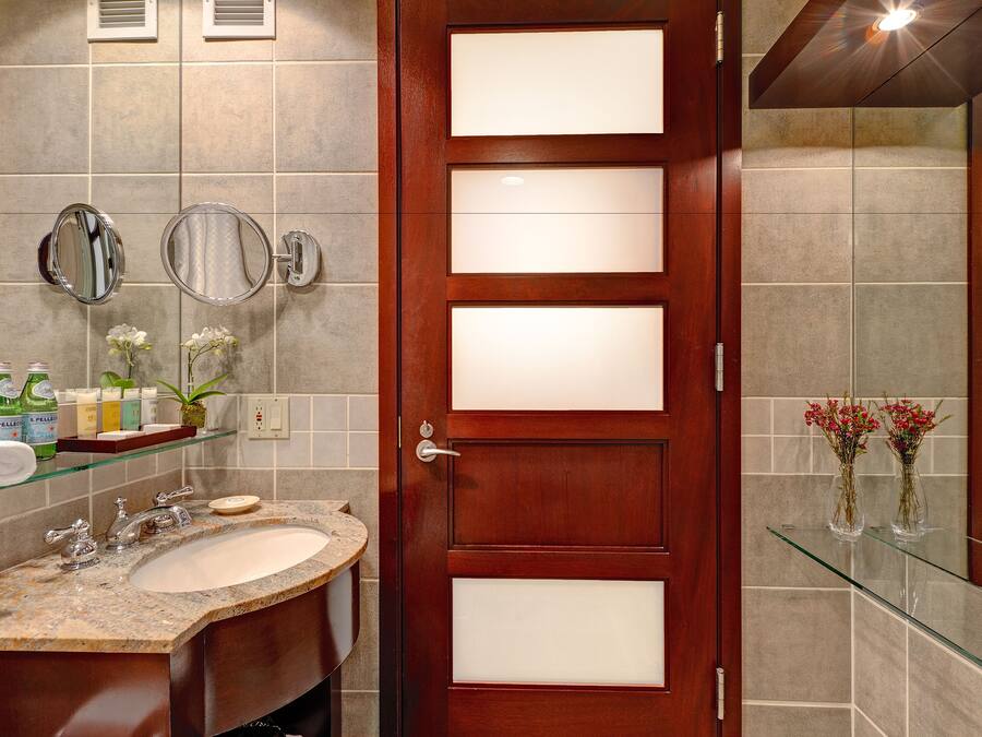 Ein Badezimmer mit Holztür, Duschkabine aus Glas, Marmorwaschbecken und zwei Spiegeln.