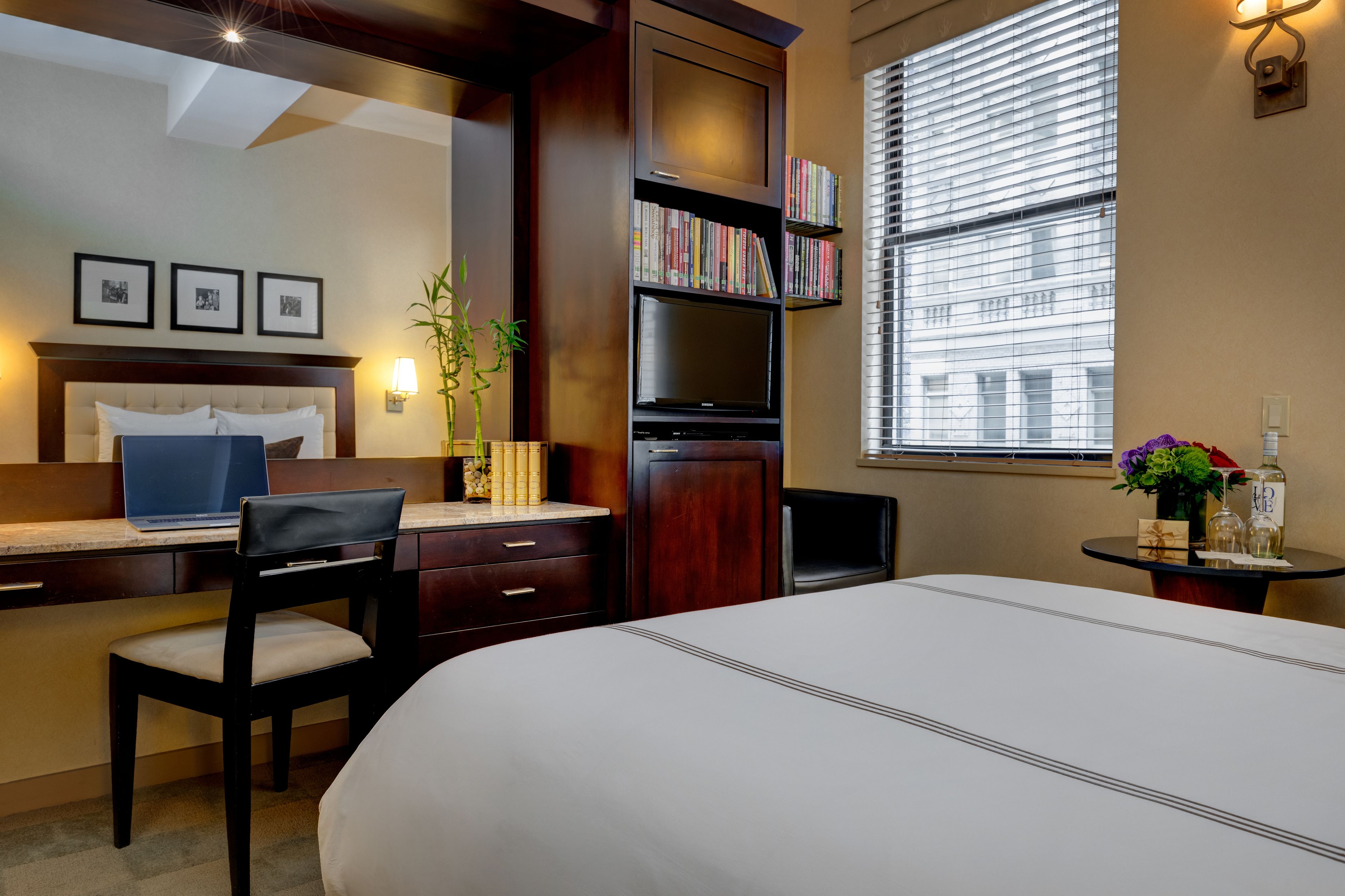 Habitación de hotel con cama, escritorio, silla, estantería y ventana con persianas.