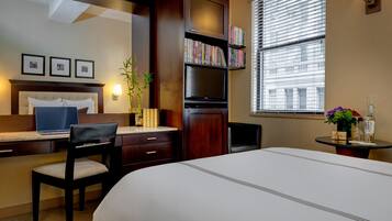 Habitación de hotel con cama, escritorio, silla, estantería y ventana con persianas.