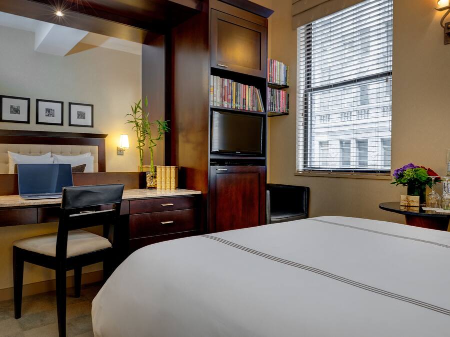Habitación de hotel con cama, escritorio, silla, estantería y ventana con persianas.