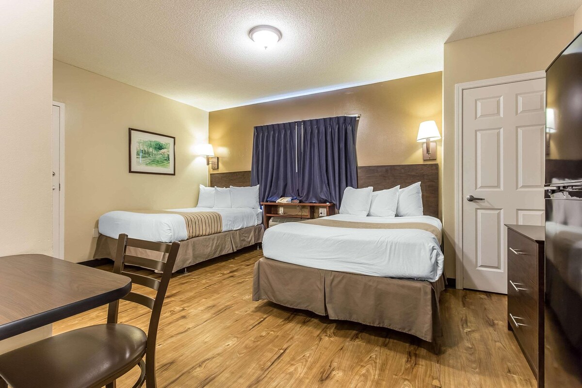 Une chambre d’hôtel avec deux lits, un plancher en bois, un bureau avec une chaise, une télévision et une porte.