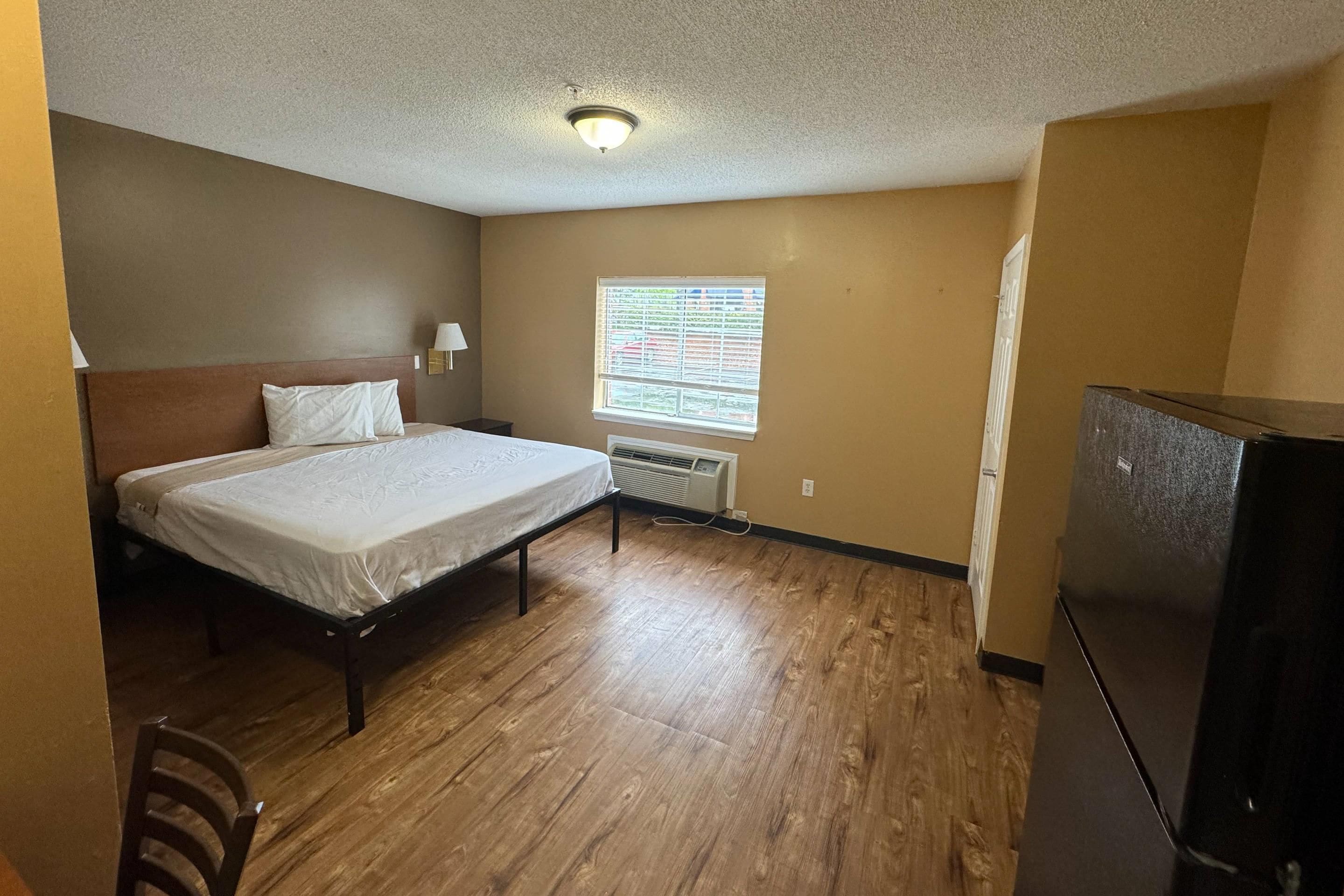 Quarto com cama, janela com persianas, radiador e frigorífico.
