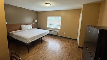 Quarto com cama, janela com persianas, radiador e frigorífico.