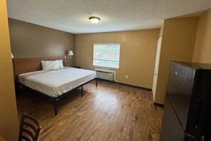 A room with a bed, a window with blinds, a radiator, and a refrigerator. - Suburban Studios near University of North Carolina-Charlotte (Charlotte)