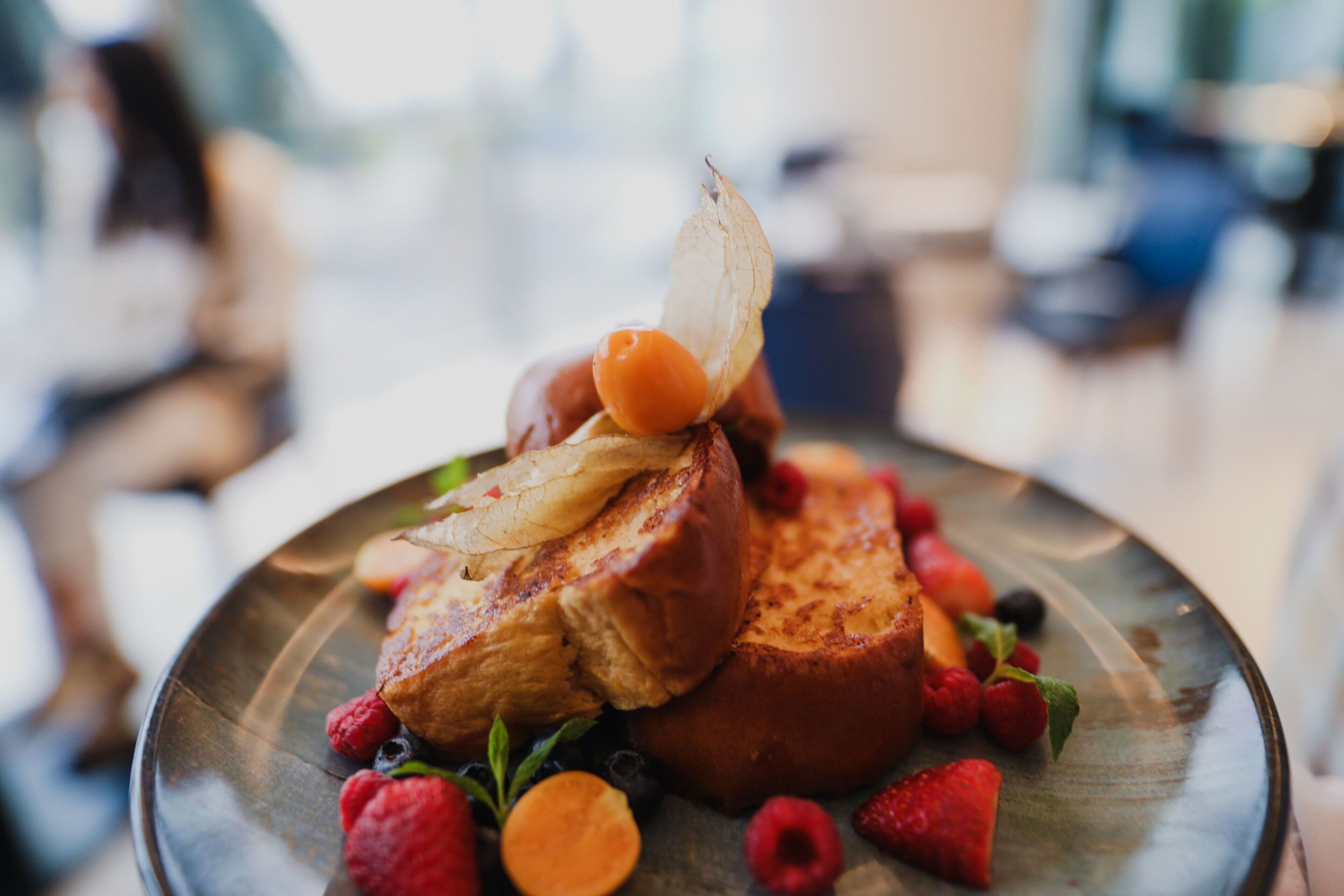 Un plato de desayuno con tostadas francesas, frambuesas y una rodaja de melocotón.