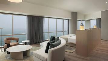 A modern hotel room with a large window, a sofa, a coffee table, and a small side table.