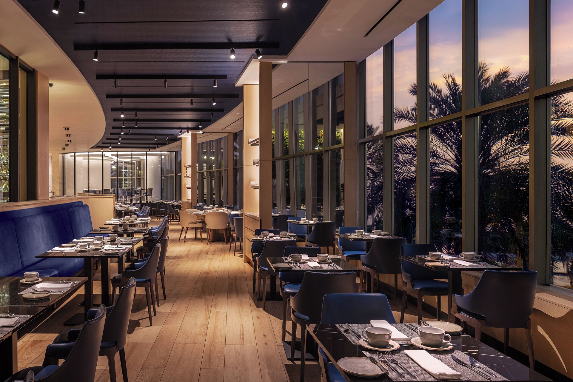 A restaurant with tables and chairs arranged along a corridor with large windows.