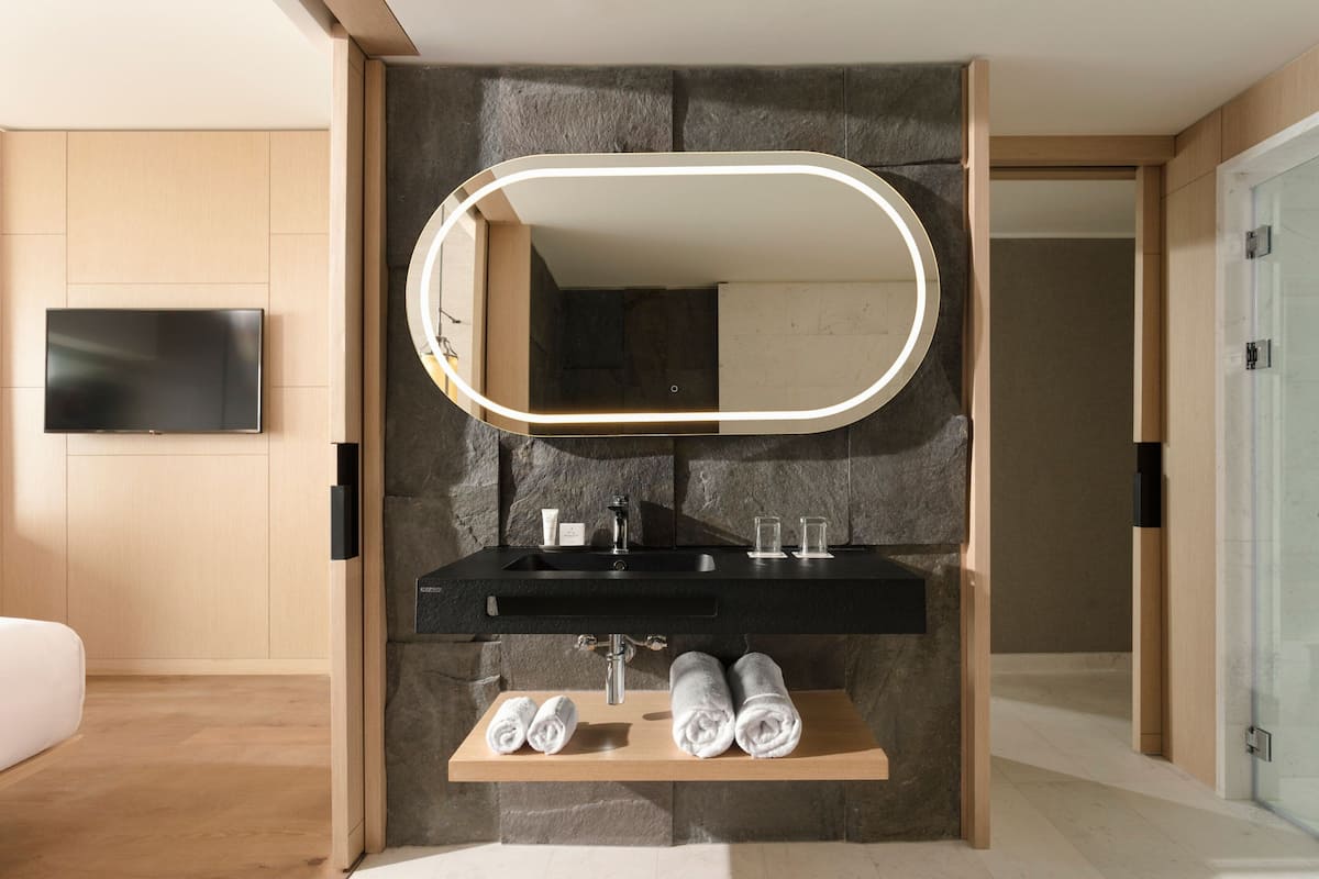 A modern bathroom with a large mirror, black sink, and wooden shelves with towels.