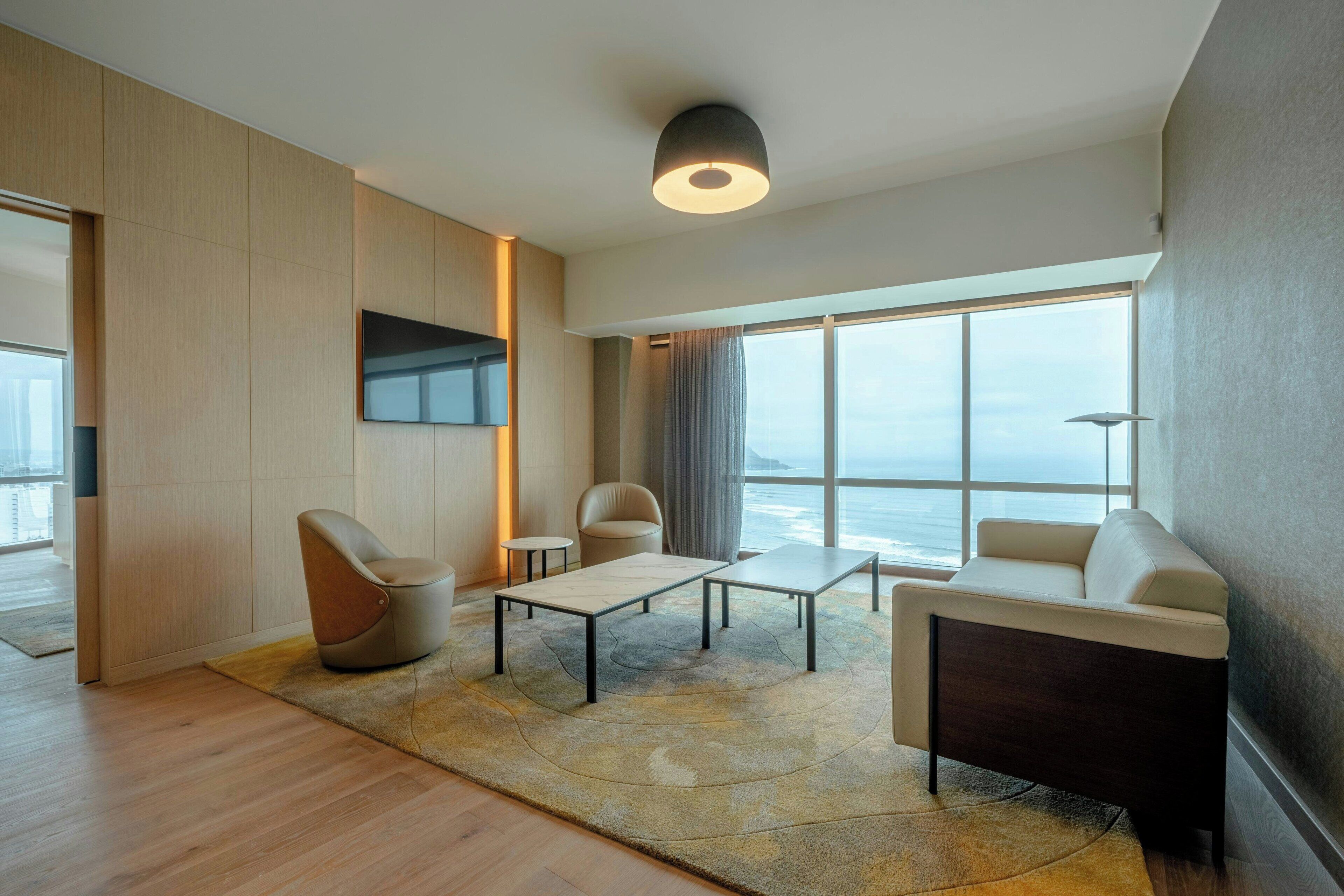 A modern living room with a sofa, two armchairs, a coffee table, and a TV mounted on the wall.