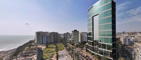 Una moderna area urbana con un edificio in vetro imponente, una struttura curvilinea e vista sul mare.