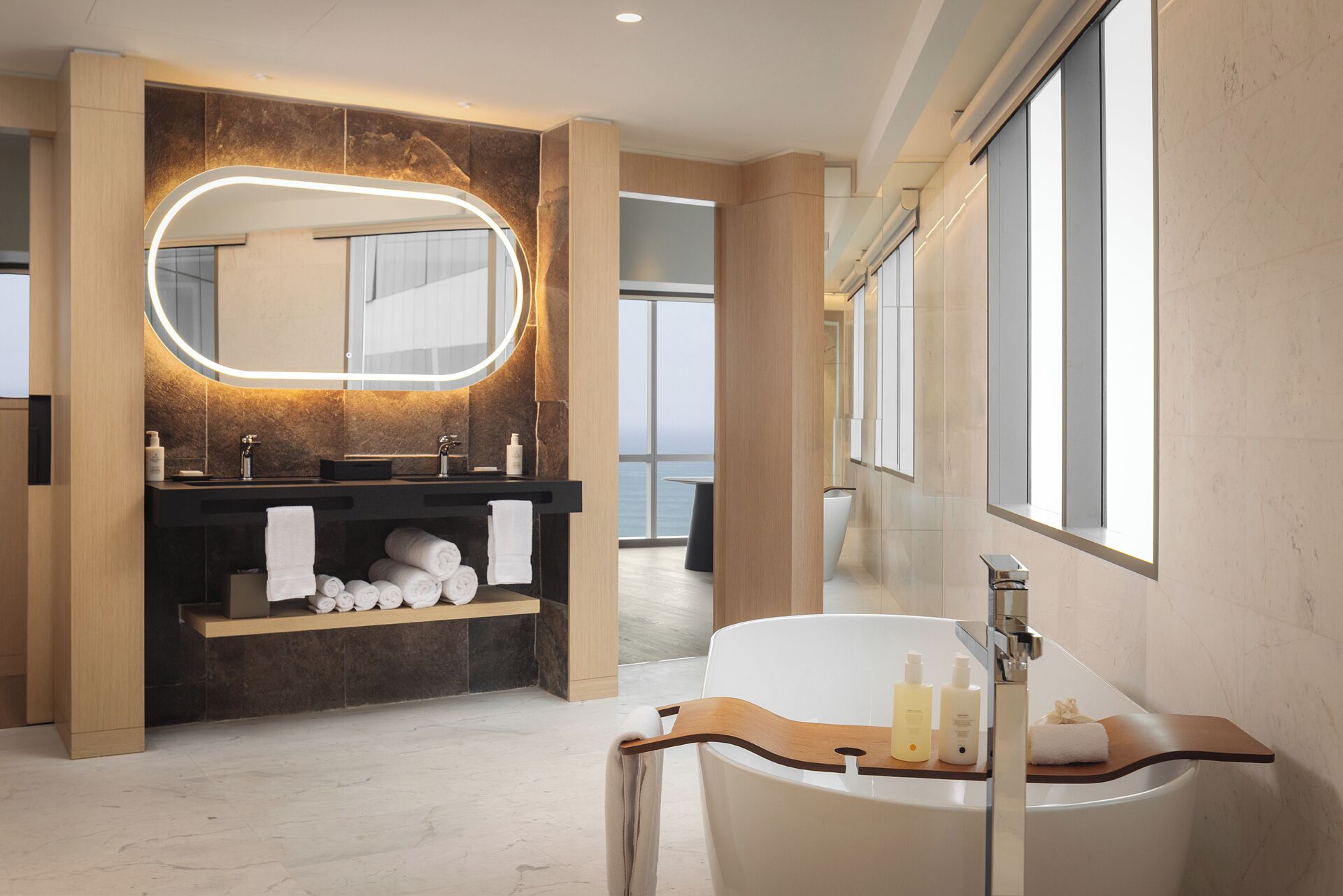A modern bathroom with a large mirror, a bathtub, and a vanity with a wooden shelf.