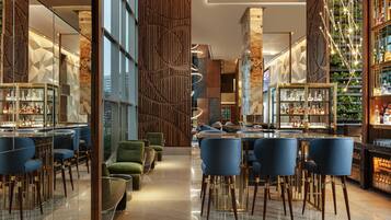 Una zona de bar moderna con estanterías de cristal, sillas azules y una mesa central.