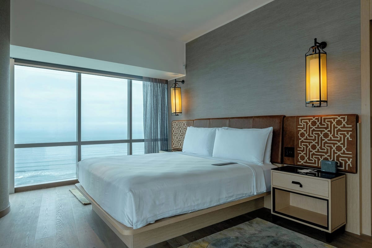 A modern hotel room with a large bed, bedside tables, and a view of the ocean.