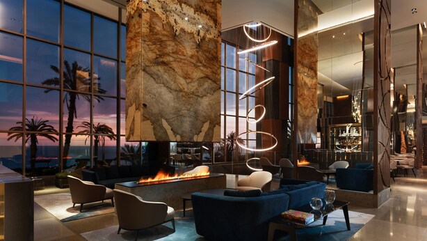 A modern lobby with a large fire feature, comfortable seating, and a view of the sunset.
