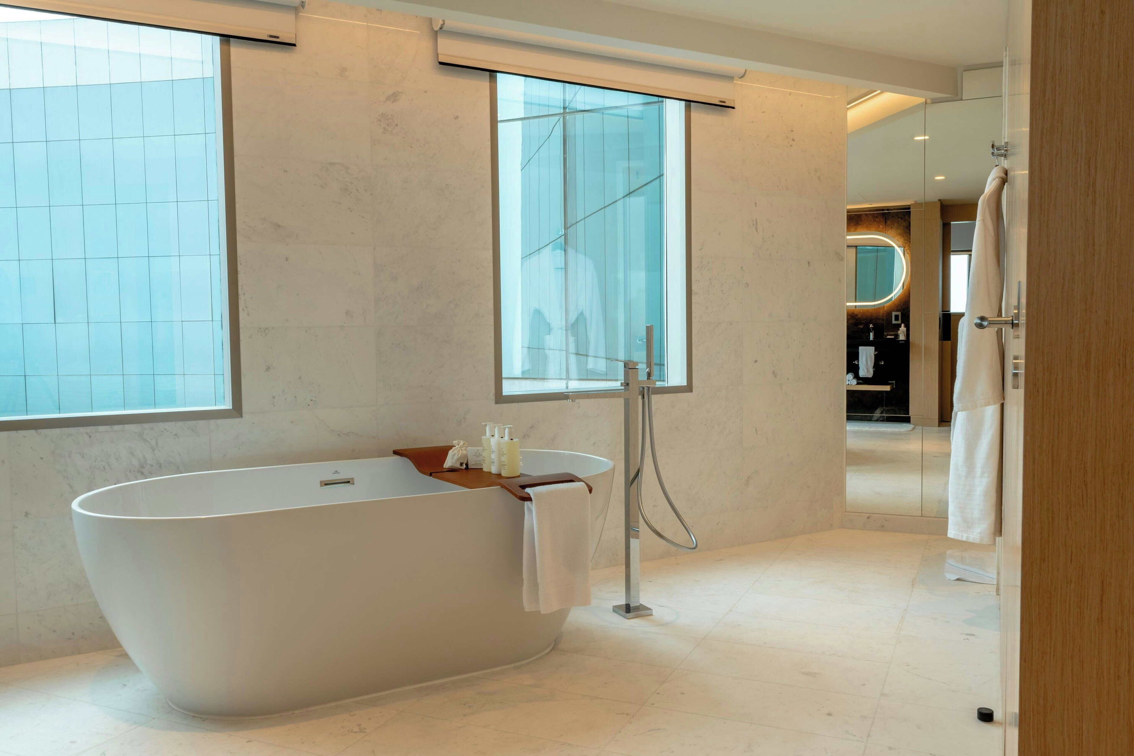 A modern bathroom with a freestanding bathtub, a large mirror, and a view of the outside through a window.