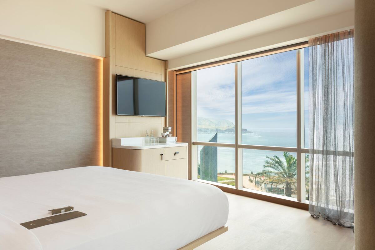 A modern hotel room with a large bed, a bathroom with a vanity, and a view of the sea.