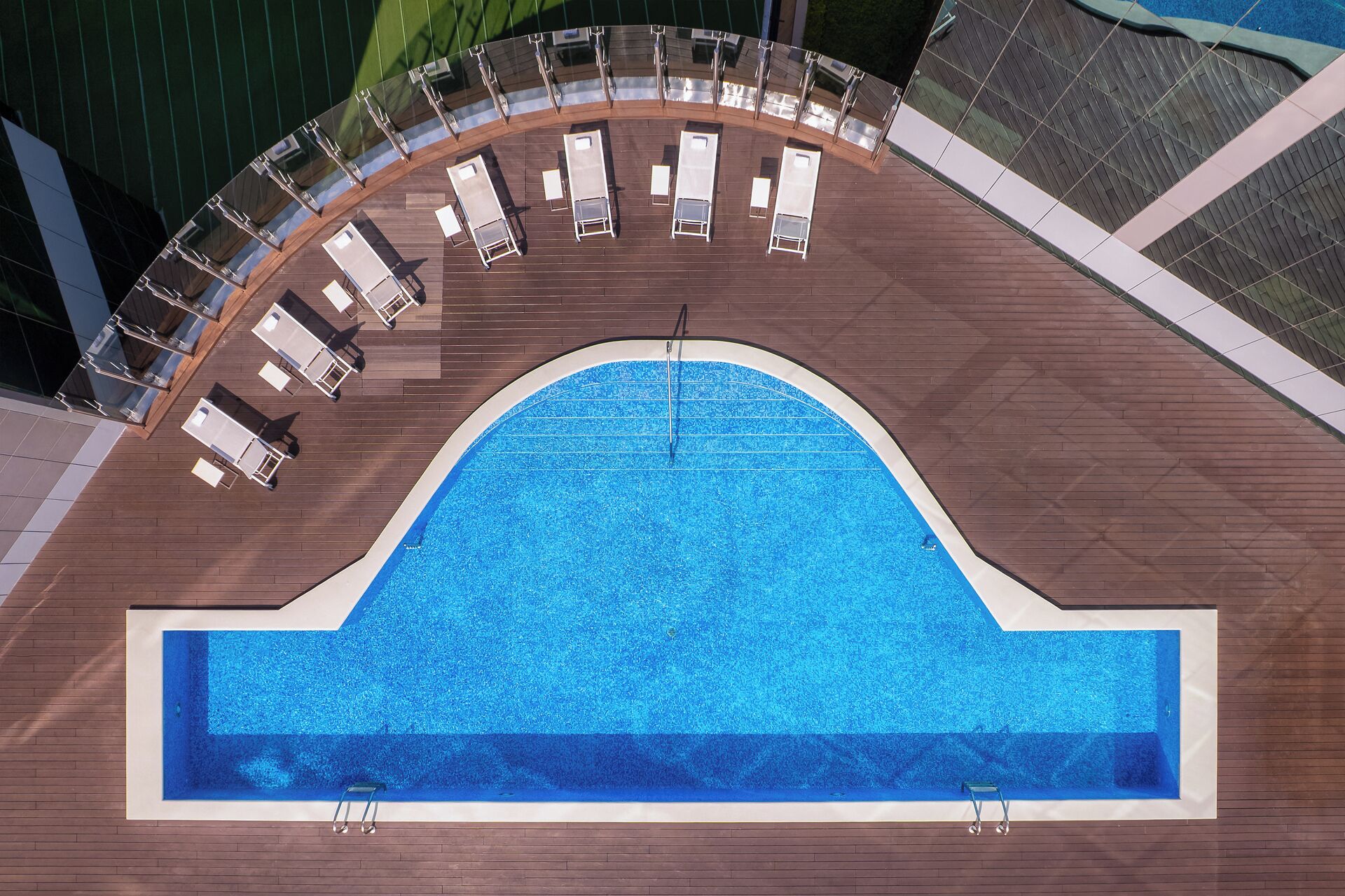 A rooftop pool with a semi-circular deck, lounge chairs, and a clear blue pool.