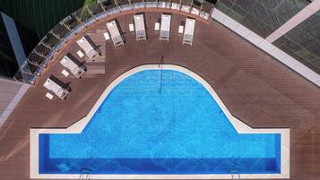 Una piscina en la azotea con un solárium semicircular, sillas de descanso y agua cristalina.