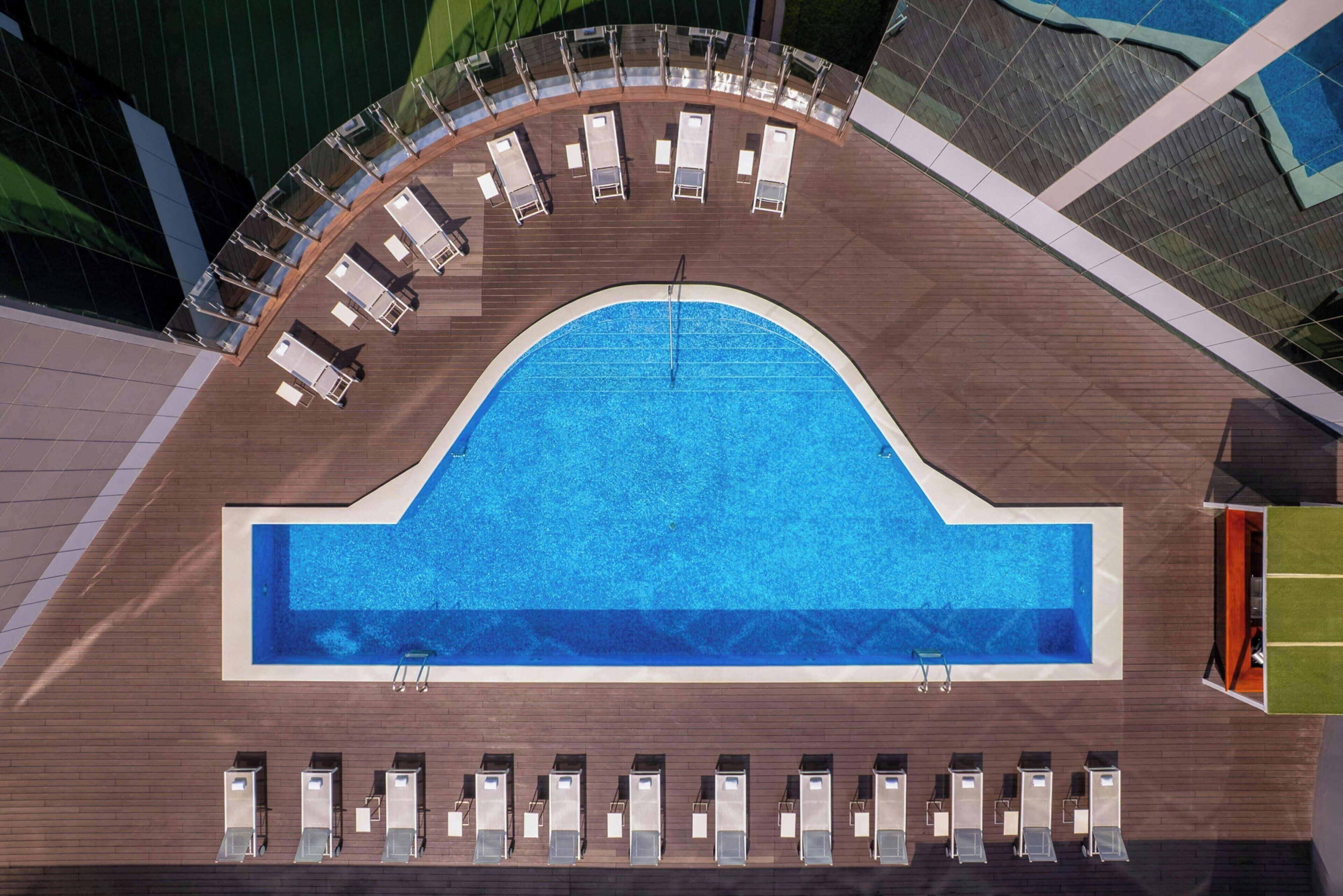 Vista aérea de una piscina con un deck semicircular, sillas de descanso y un diseño arquitectónico moderno.