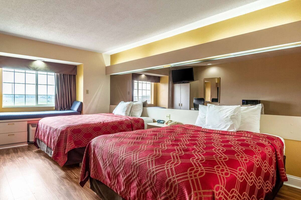 Habitación de hotel con dos camas, un escritorio, una silla, un televisor y una ventana con cortinas.