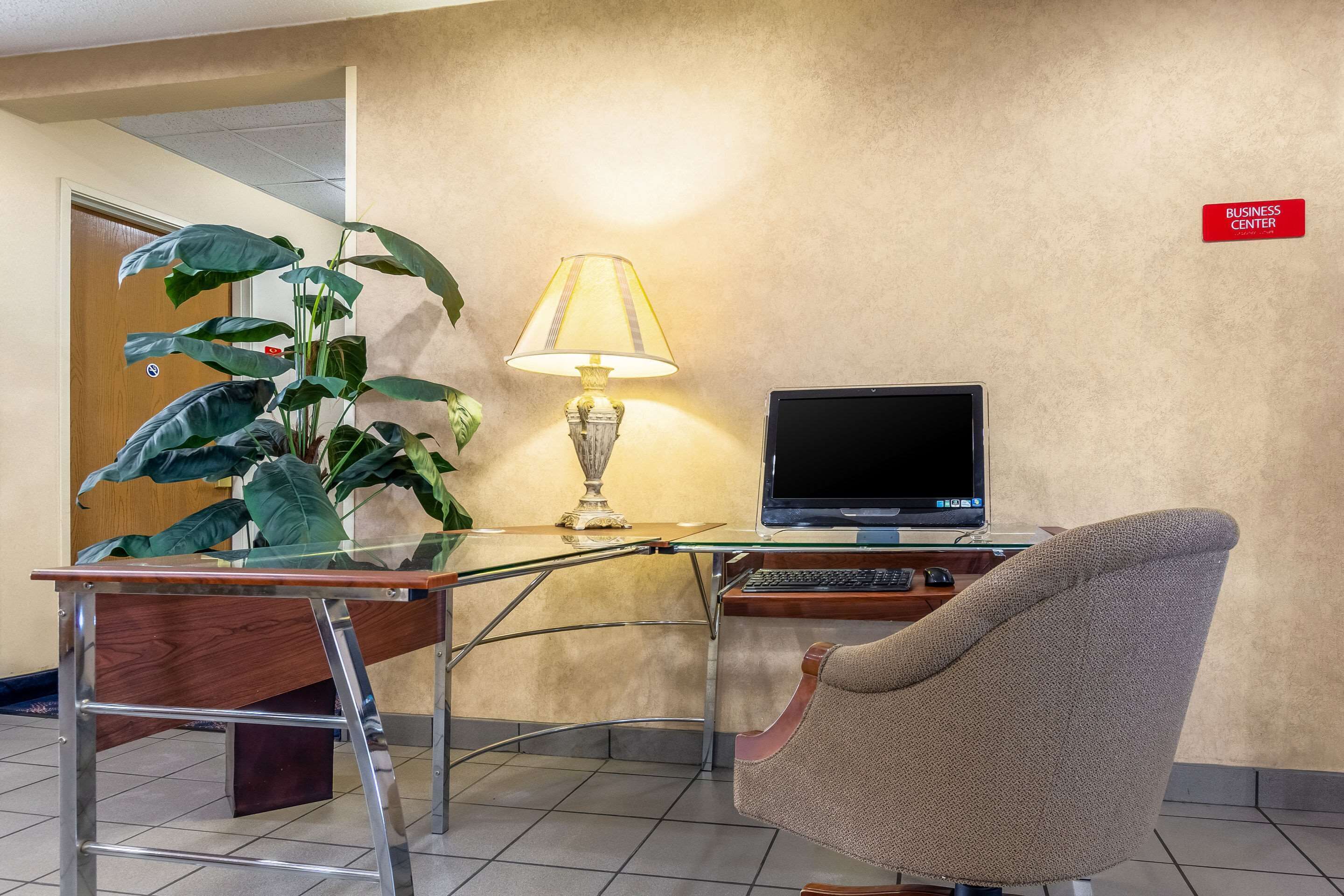 Un centre d’affaires équipé d’un bureau, d’un ordinateur, d’une chaise, d’une lampe et d’une plante.