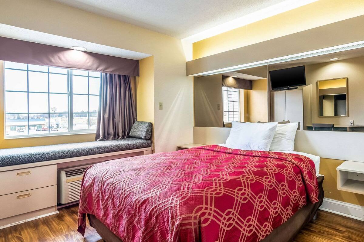Una habitación de hotel con cama, un asiento junto a la ventana, escritorio y televisión.