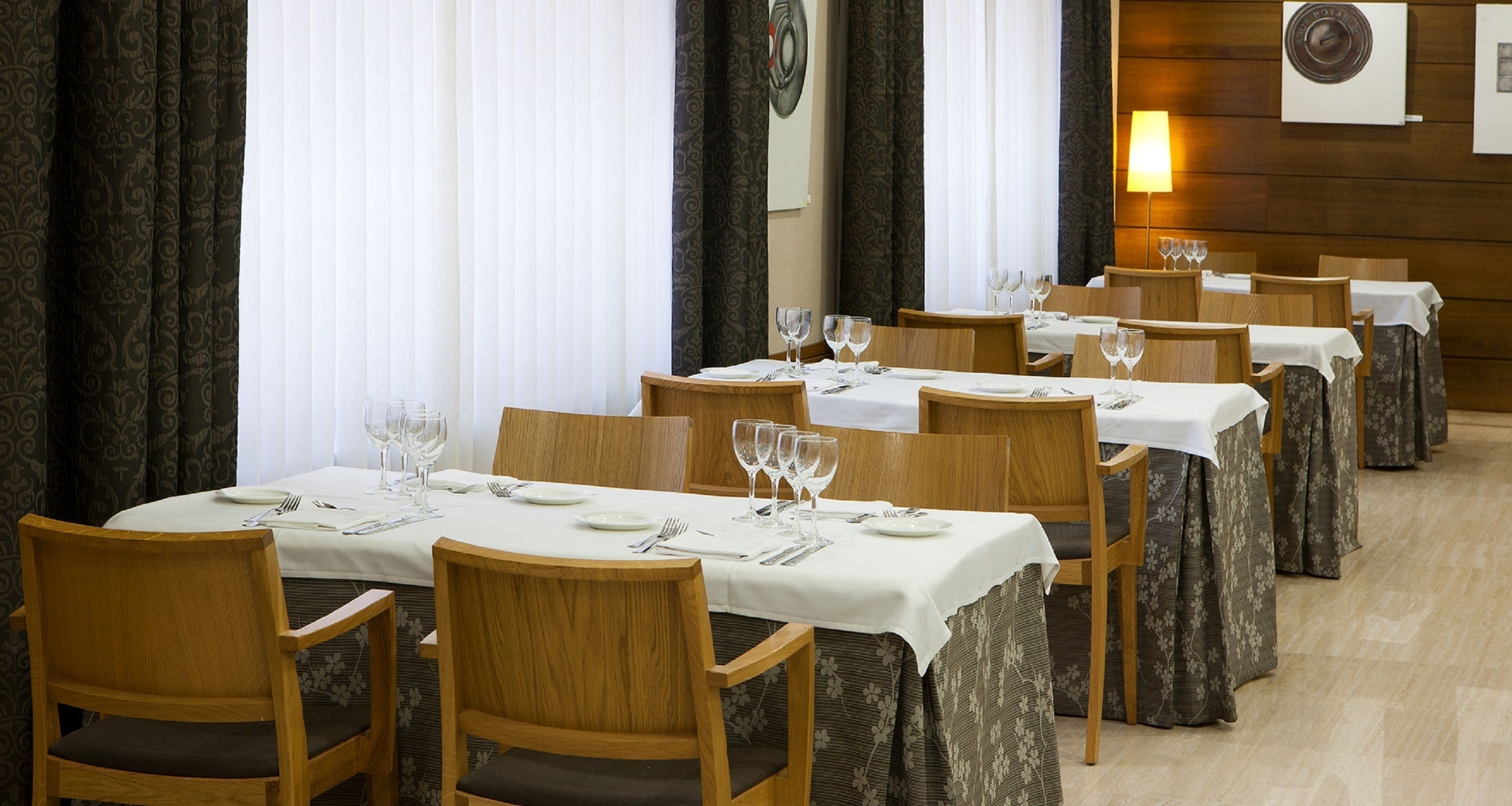 Un restaurant avec de nombreuses tables dressées pour le service, des chaises en bois et une lumière douce et chaleureuse.